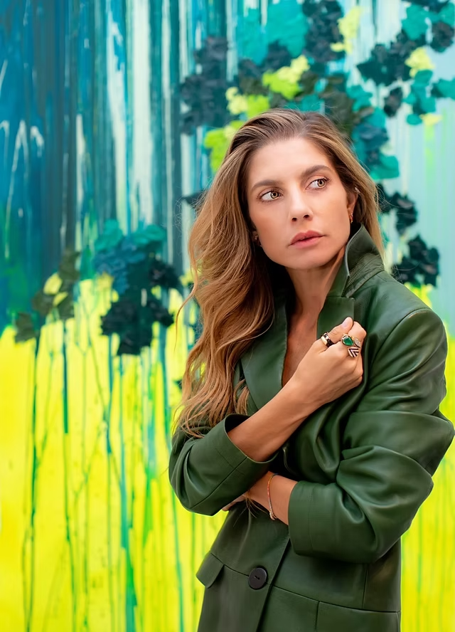 Woman in a green coat standing in front of a colorful abstract wall.