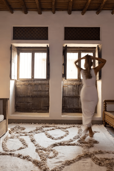 A woman standing on the Woven For Him rug by Moe Khadra, showcasing its elegant design in a cozy interior.