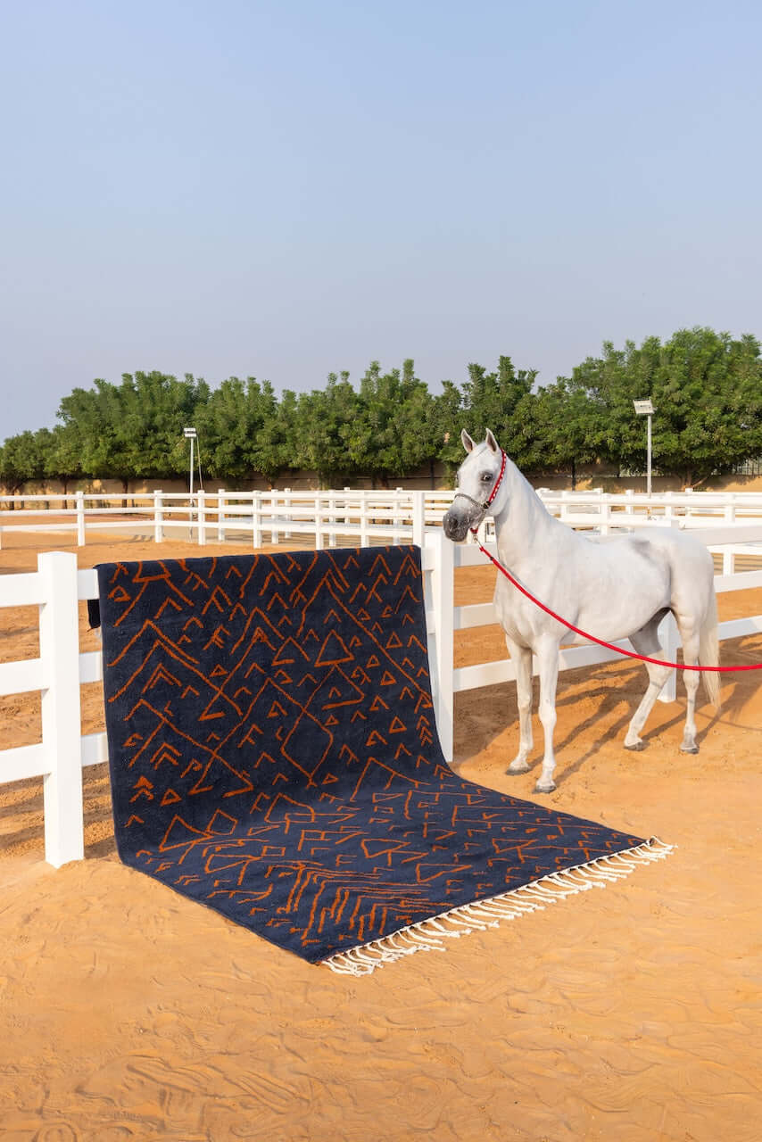 Amara Nuit - The mystique of Moroccan night rug displayed beside a white horse in an outdoor riding arena.