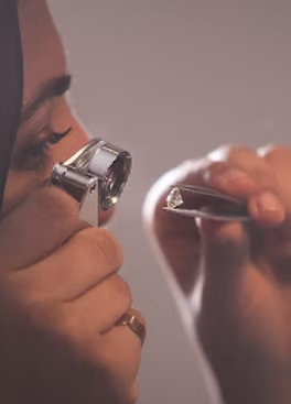 Person holding a diamond between two hands with a magnifying glass.