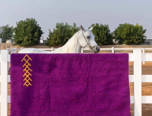 Sahara Gaze – Moroccan Rug with Golden Motifs draped over a fence with a white horse in the background.